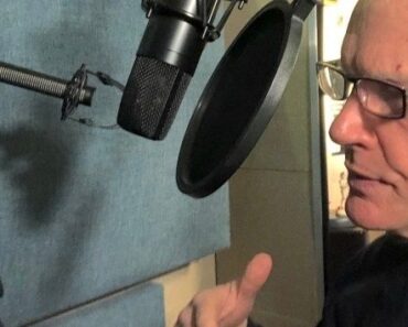 Mies puhuu studiossa mikrofonin ja pop-filtterin edessä